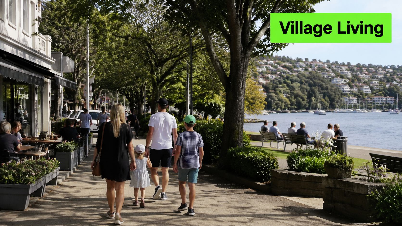 A family walks along a sunny waterfront promenade in a scenic coastal village with hillside homes.